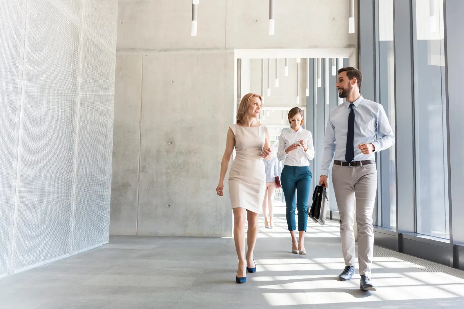 A group of businesspeople talking while walking through a bright hallway.
