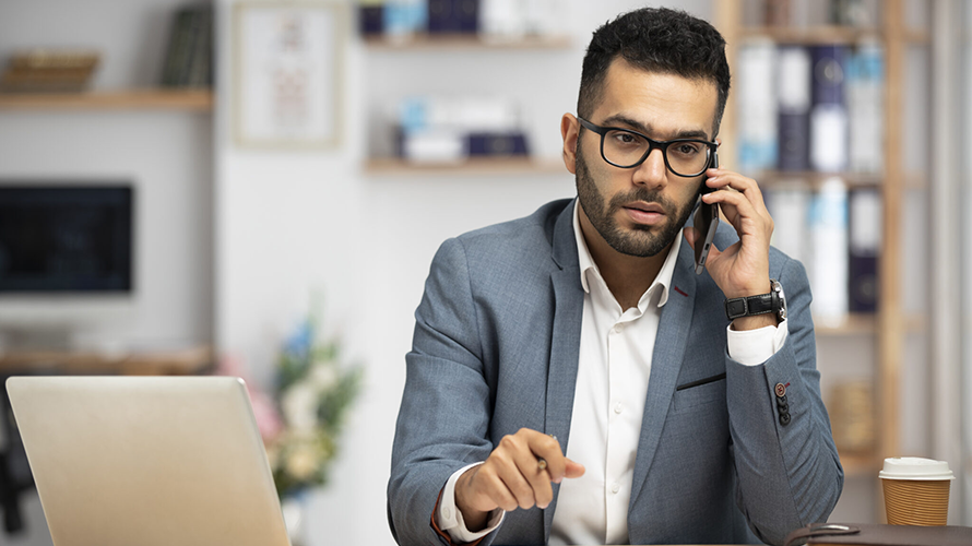 A businessman on a mobile phone at his desk.